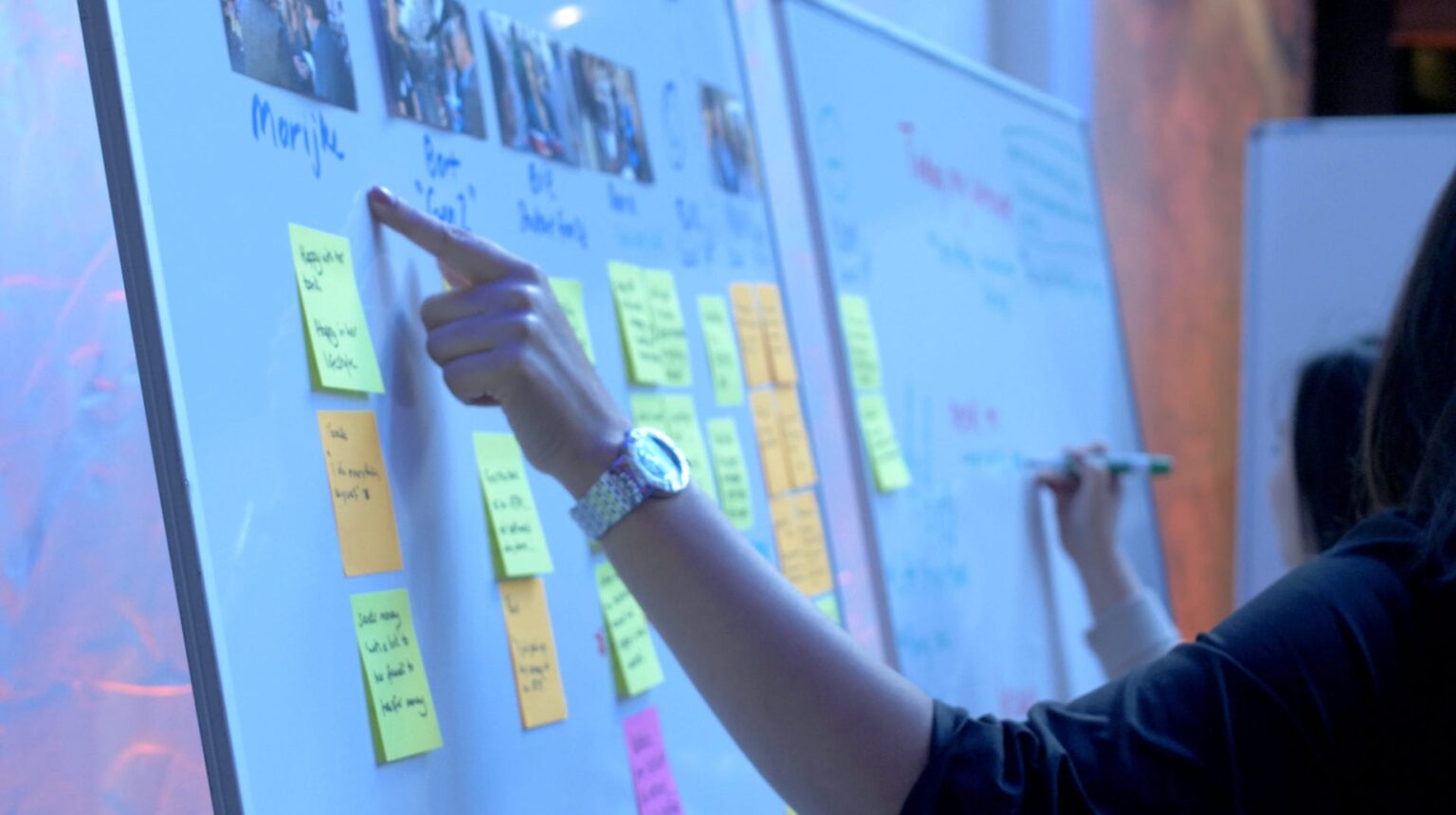 A person pointing to sticky notes on a wall.