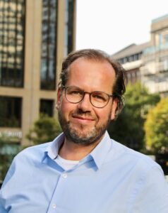 A man with glasses and beard wearing a blue shirt.