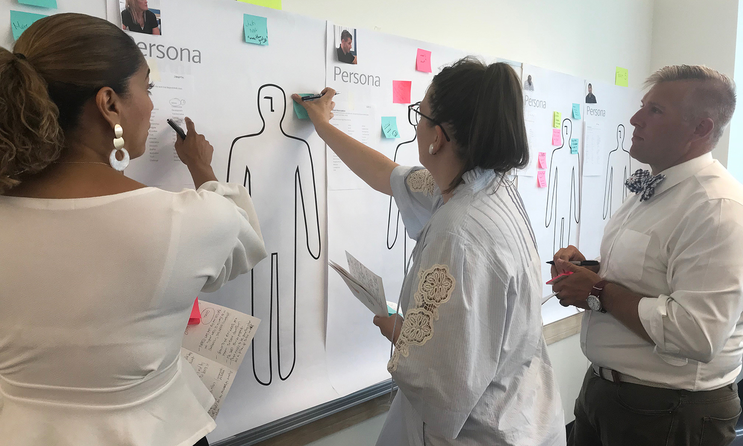 A group of people standing around a wall with sticky notes on it.